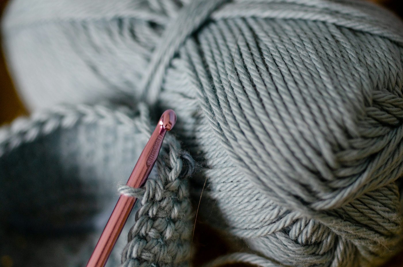 A pink crochet hook working into grey crochet stitches