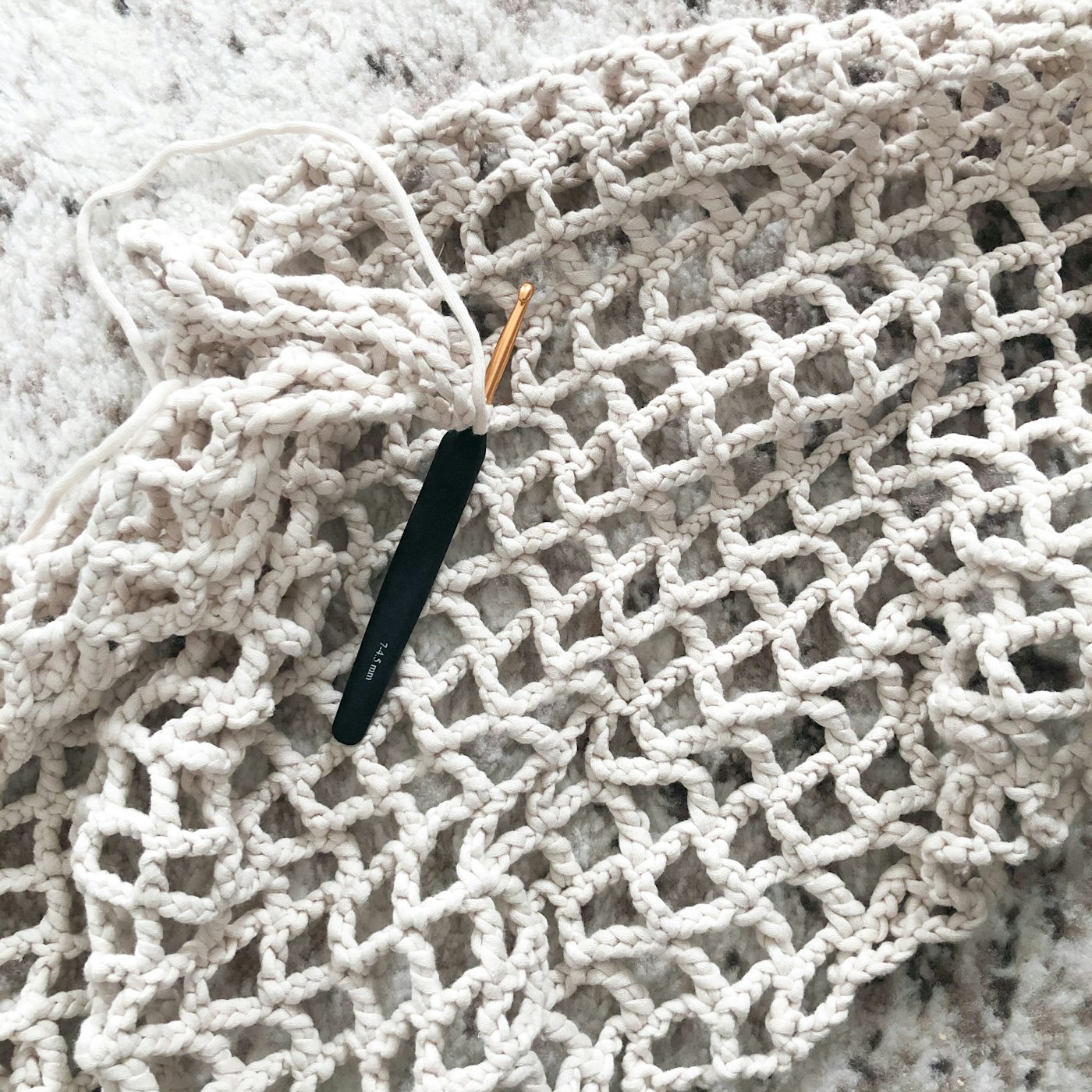 A crochet hook resting on white crocheted chain mesh