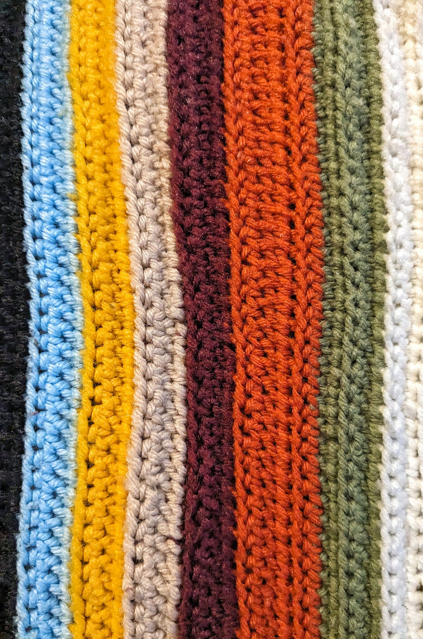 Close-up of crochet stitches in vertical stripes of blue, mustard, rust and grey