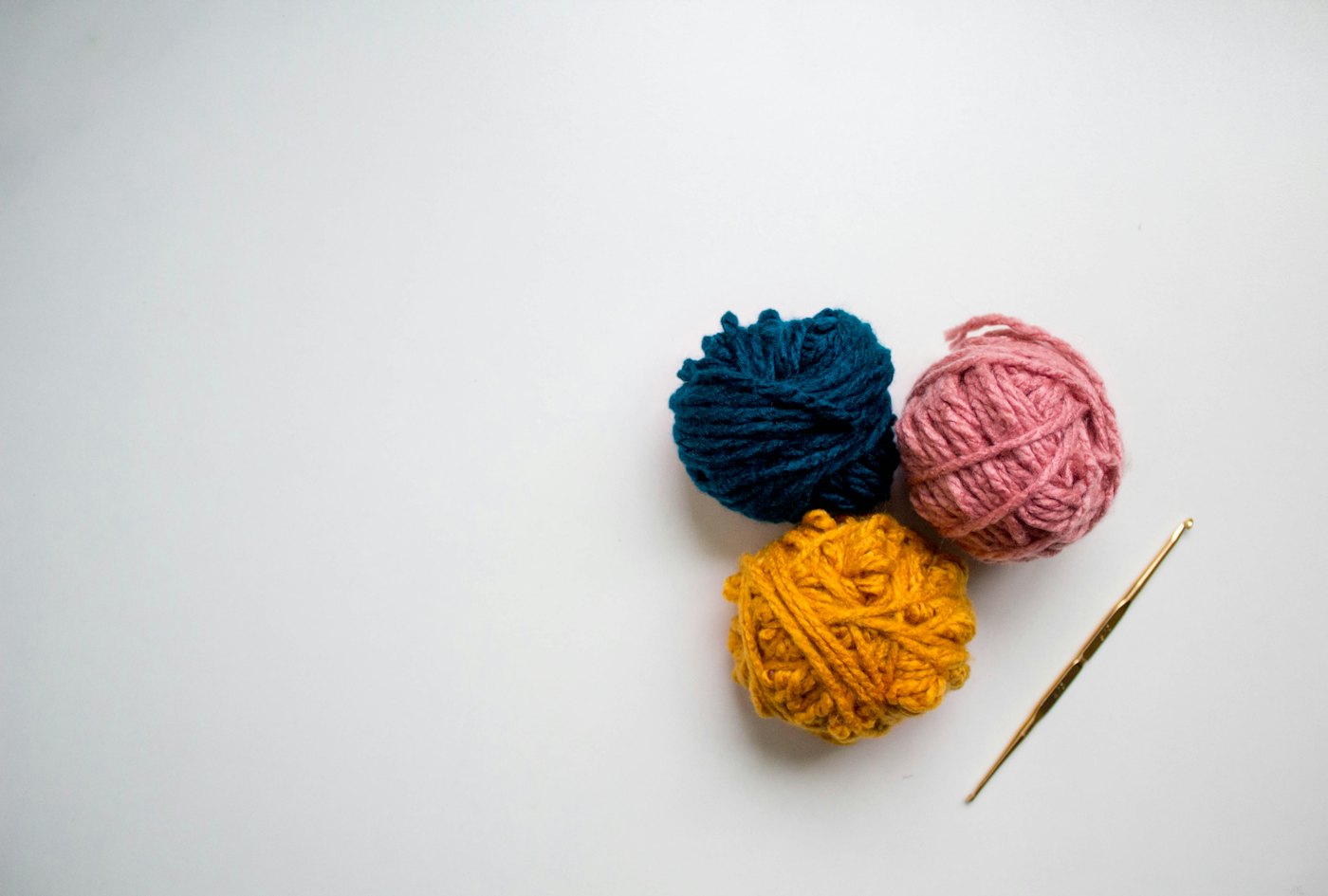 Three small balls of navy, red and mustard yarn next to a crochet hook